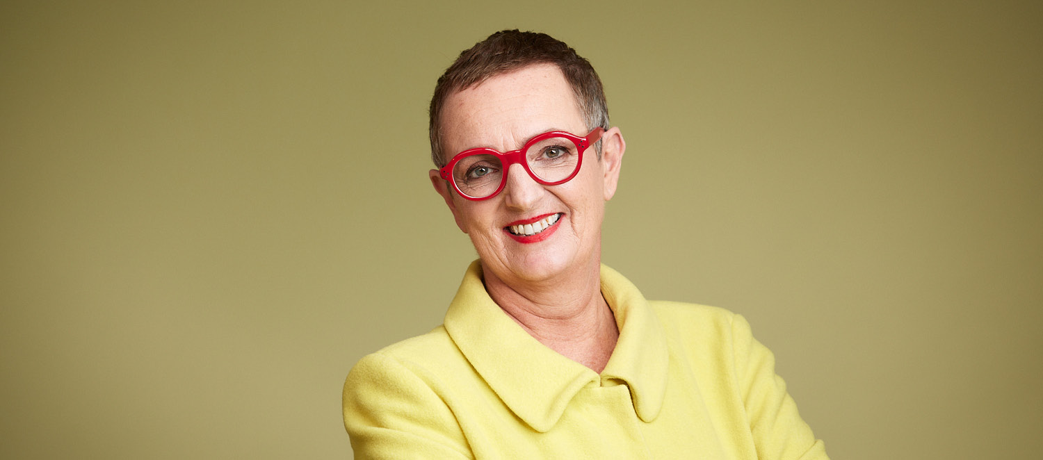 Porträtfoto: Irene Wagner. Zu ihren raspelkurzen Haaren trägt sie eine rote Brille und eine gelbe Jacke.