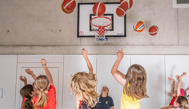 In einer Sporthalle: Mehrere Mädchen werfen Bälle auf einen Basketballkorb. 