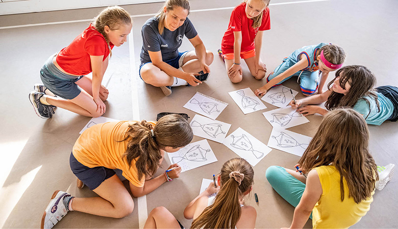 Julia Harms und die U10-Mädchen sitzen im Kreis; die Mädchen beschriften Papierbögen.