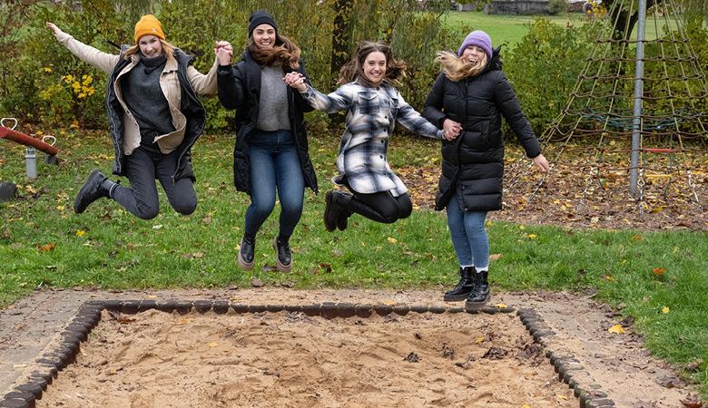 Auf einem Spielplatz. Lisa-Marie Schmitt und drei andere junge Frauen halten sich an den Händen und springen hoch.