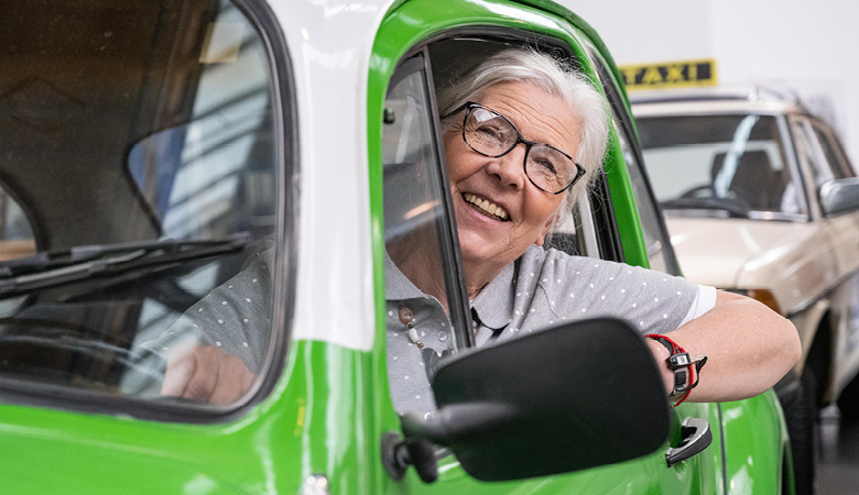 Marianne Schweinesbein sitzt am Steuer eines grasgrünen alten VW Käfer. Strahlend schaut sie aus dem Fenster.