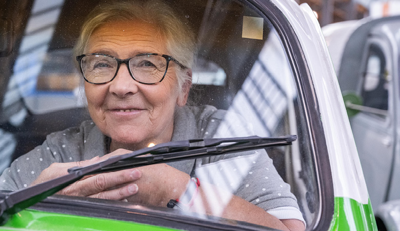 Marianne Schweinesbein am Steuer des Käfers. Sie lächelt verschmitzt.