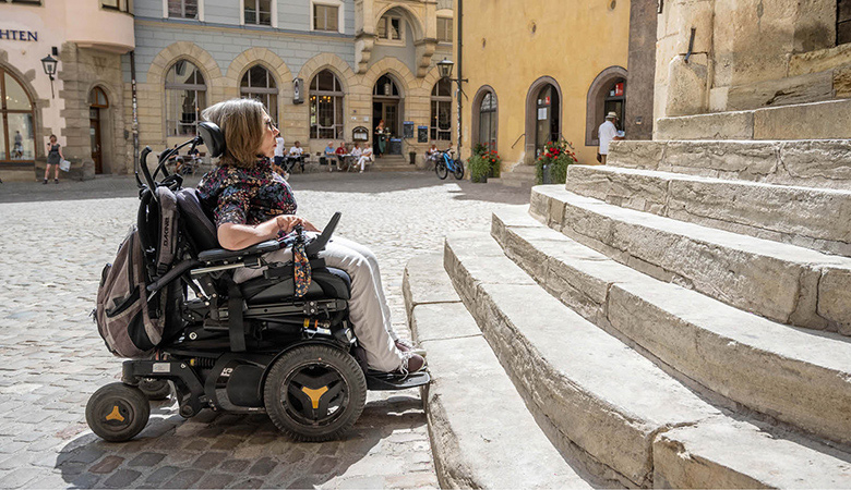 Wiebke Richter steht mit ihrem Rollstuhl vor den Stufen des Regensburger Rathauses.
