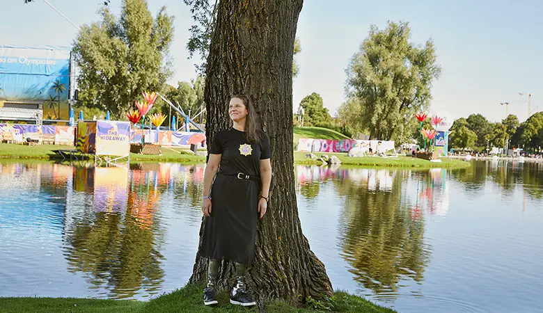 Frau lehnt an einem Baum vor einem Teich. 