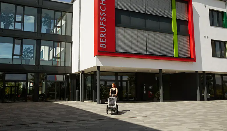 Frau mit einem Kinderwagen vor einem Bürogebäude. 