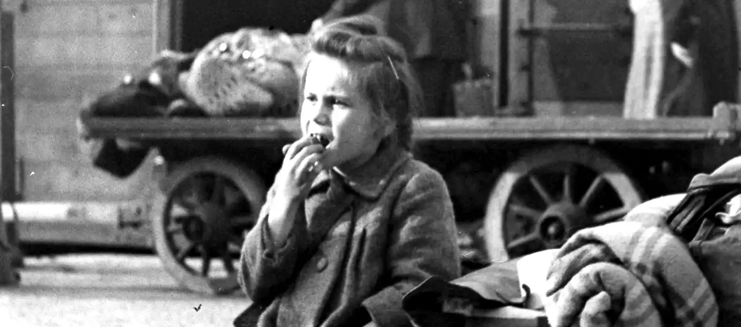 Evakuiertes Flüchtlingsmädchen sitzt auf einem Wagen mit Essen in der Hand, 1947