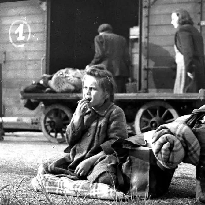Evakuiertes Flüchtlingsmädchen sitzt auf einem Wagen mit Essen in der Hand, 1947
