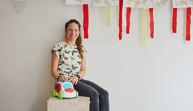 Frau sitzt auf einer Kiste mit einem Spielzeugauto aus Stoff vor sich