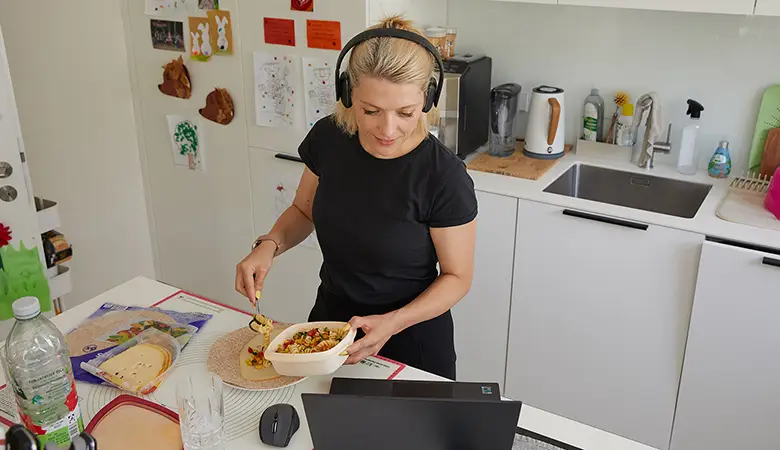 Frau beim Zubereiten einer Lunch-Box mit Blick auf einen Laptop.